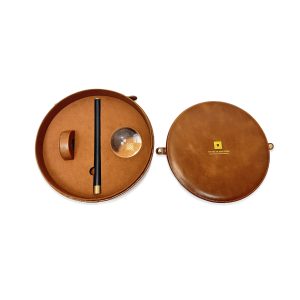 A premium circular brown leather carrying case with a gold clasp on a minimalist white background.